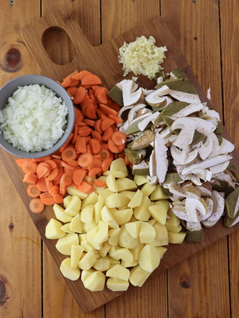 Image of sliced ingredients for porcini soup: onions, garlic, porcini mushrooms, carrots and potatoes